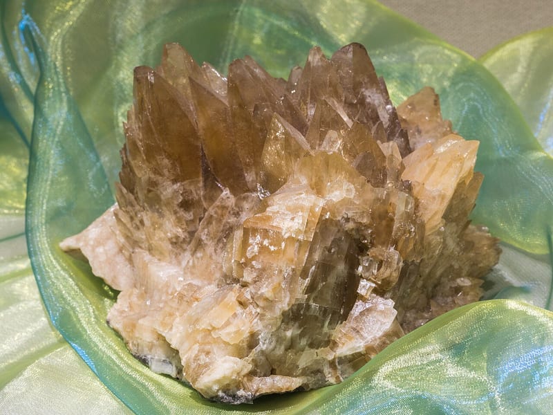 Kelompok kristal kalsit berwarna krem kecokelatan di atas kain hijau.