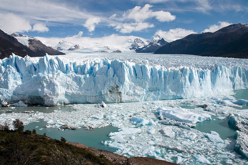 Dinding es Gletser Perito Moreno yang retak-retak menghadap perairan dengan bongkahan es terapung.